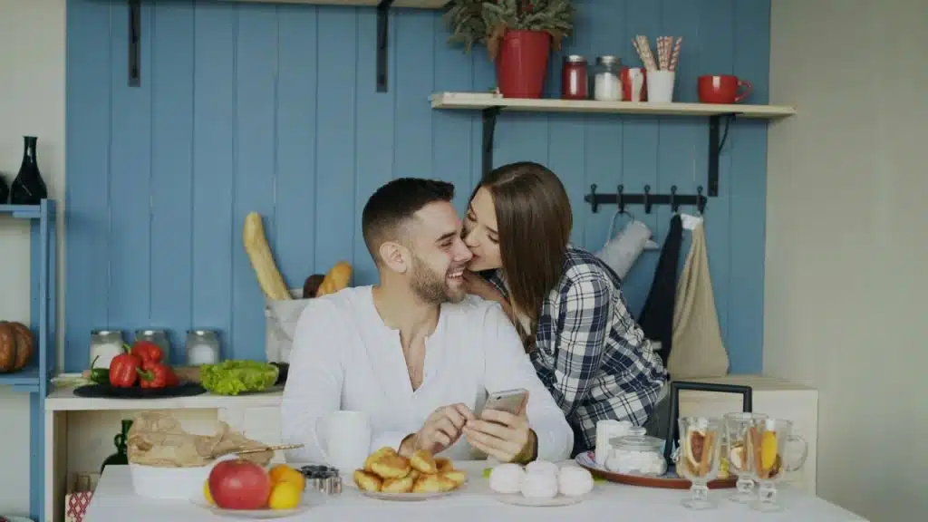 A woman kissing her husband in the kitchen