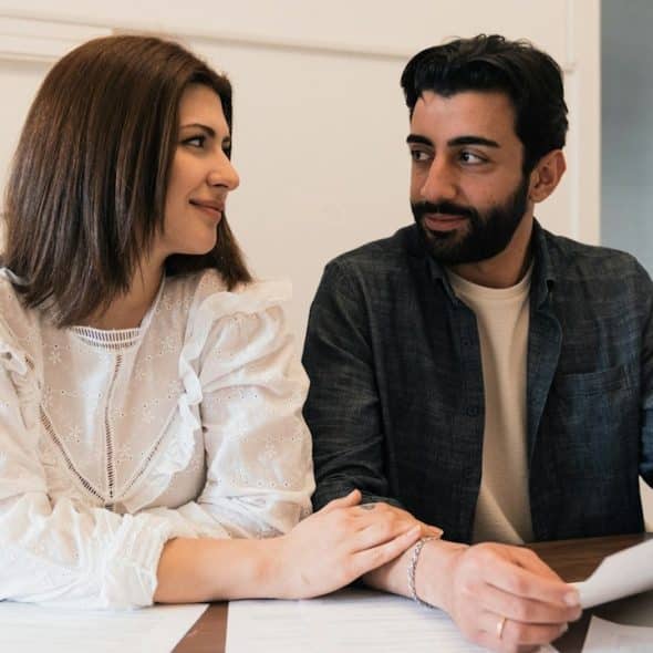 A smiling woman looking at a bearded man and placing her hand on his arm while he holds a document.