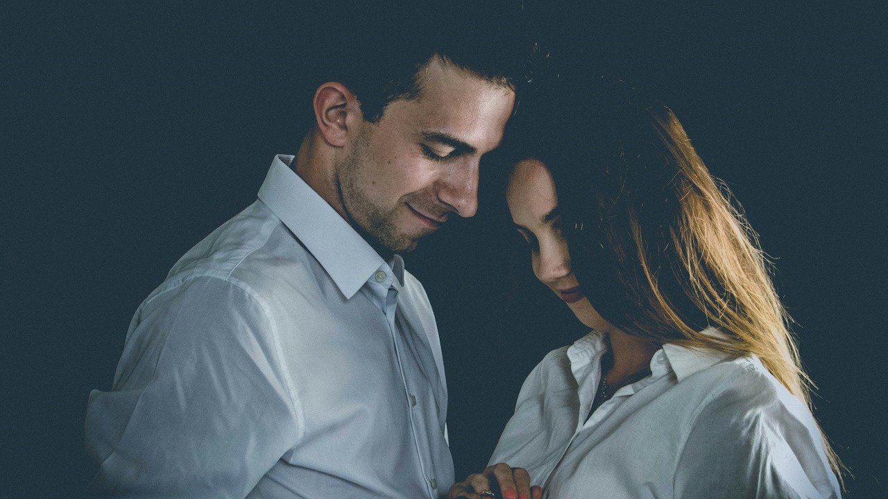A couple smiling while standing near each other and gazing downwards.