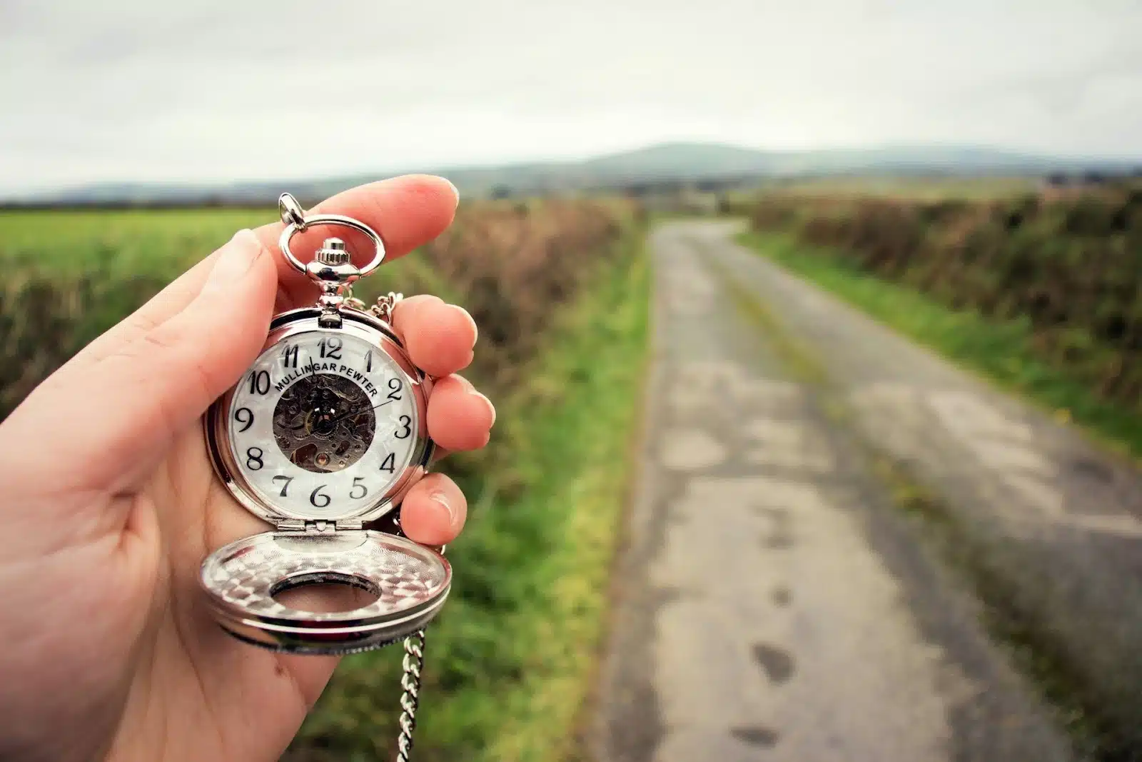 A pocket watch with a blurred road and field at the background