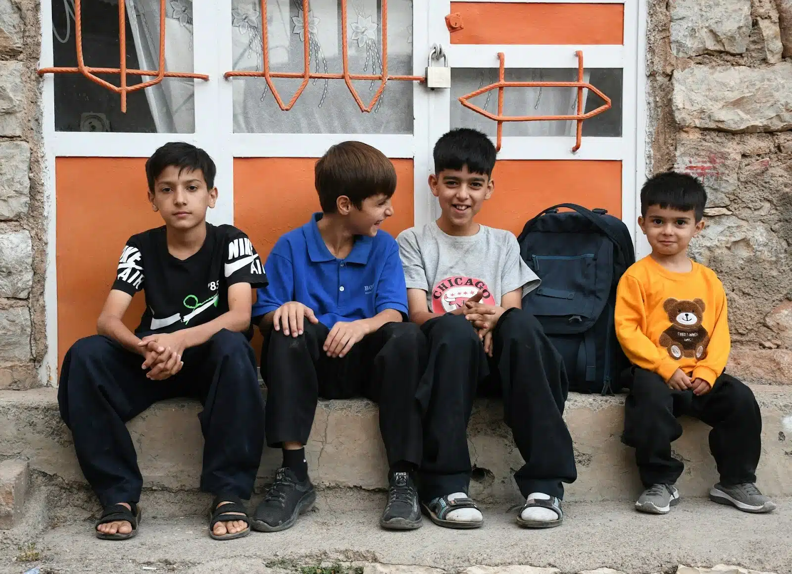 A diverse group of young boys sitting on a sidewalk