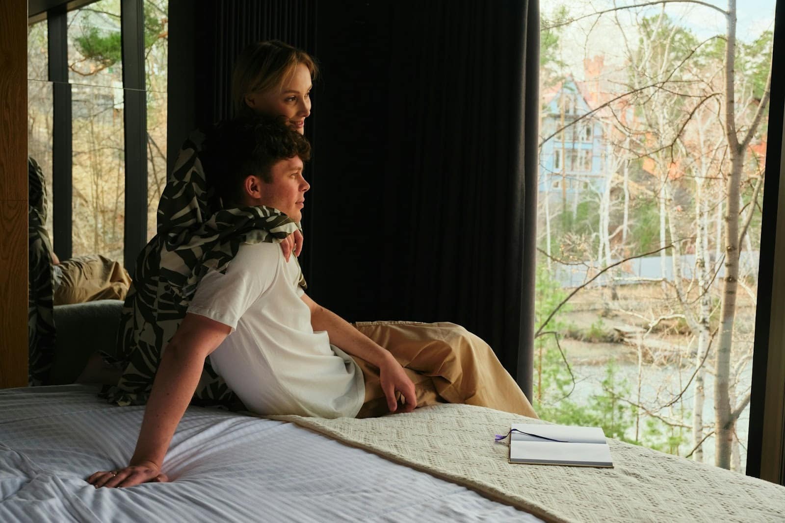 A couple sitting on their bed by the window