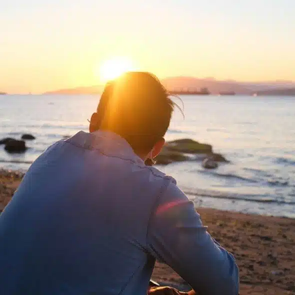 A person sitting on a rocky beach watching the sunset over the water.