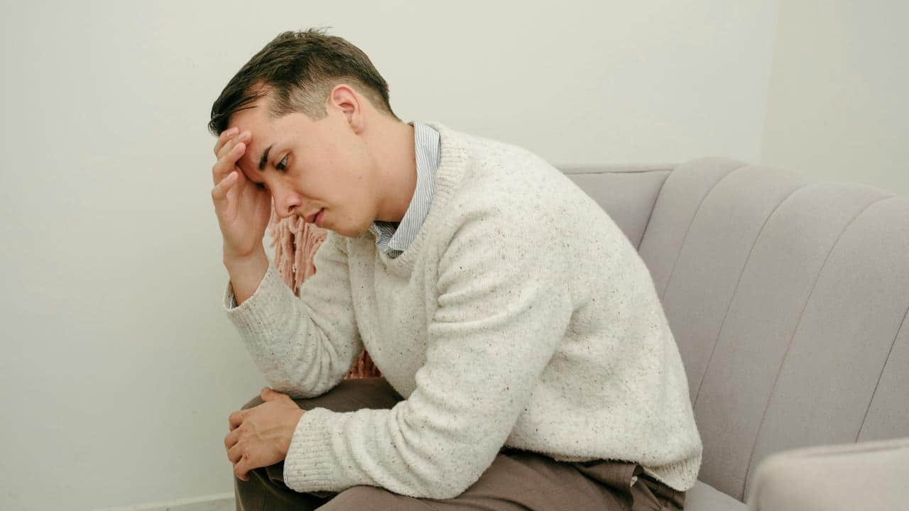 A man sitting on a couch with his head in his hand looking stressed.