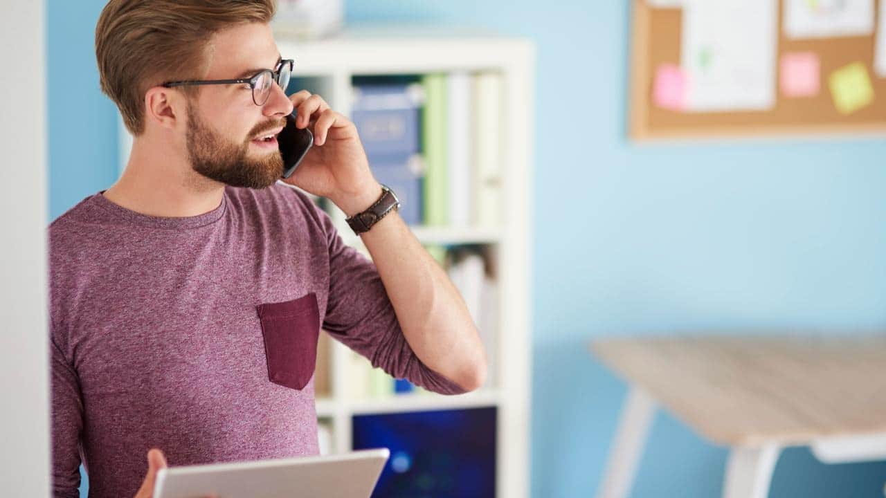 A man holding a tablet while talking on a phone in an office.