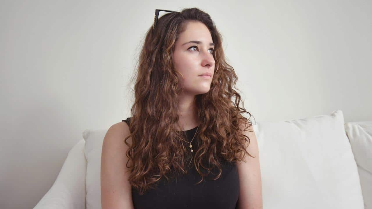 A woman with curly hair sits on a couch and looks off to the side.