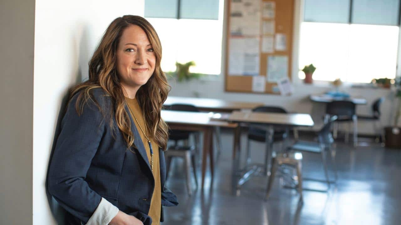 A woman smiles while leaning against a wall in an office setting.