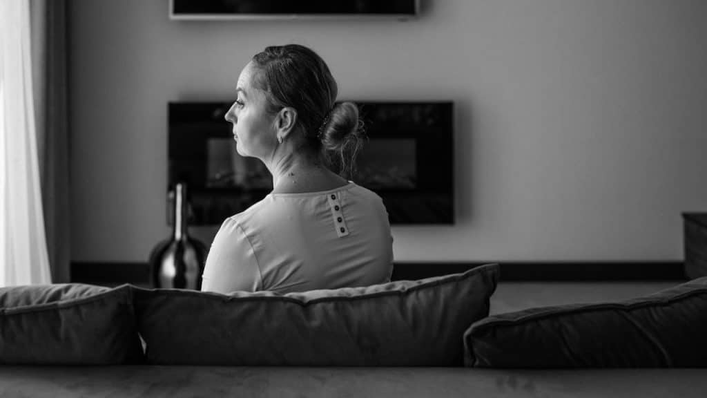 A black and white photo shows a woman from behind, sitting alone on a couch.