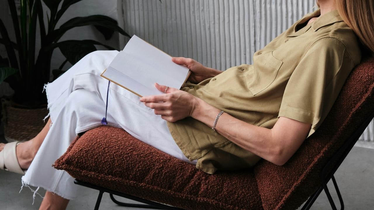 A person reclines in a chair while reading an open book indoors.