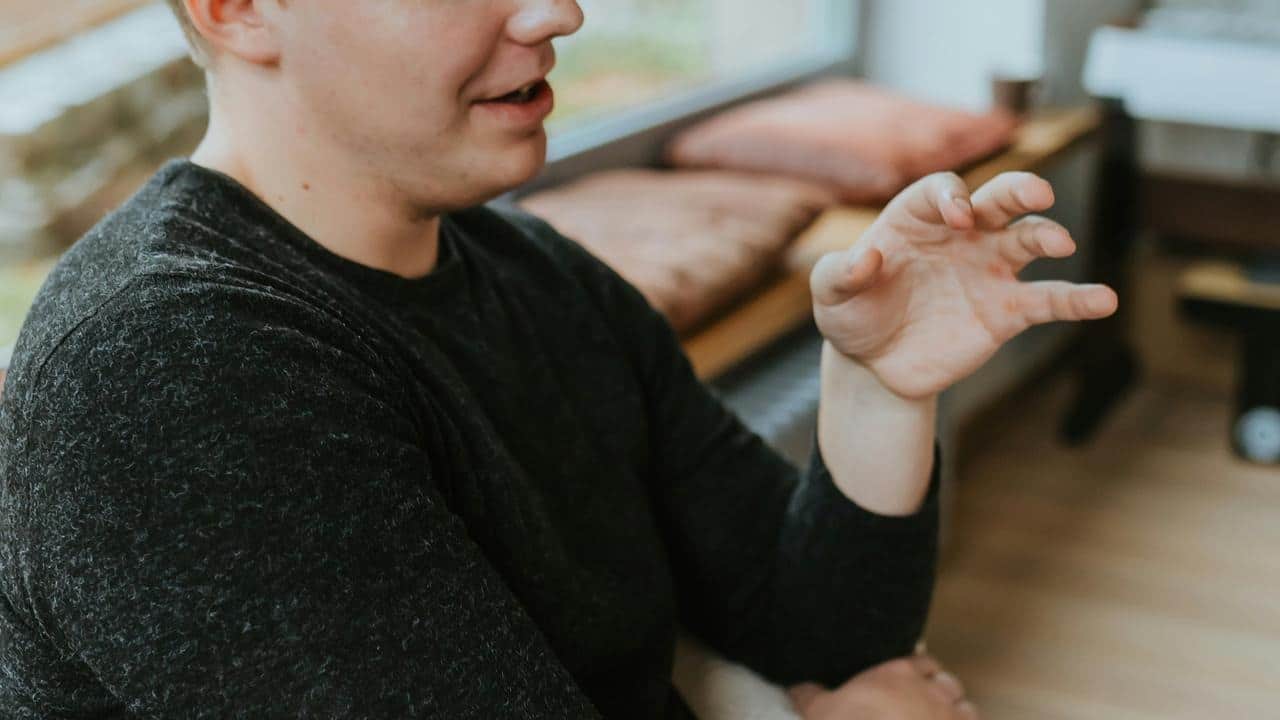 A man gestures with his hand while talking indoors.