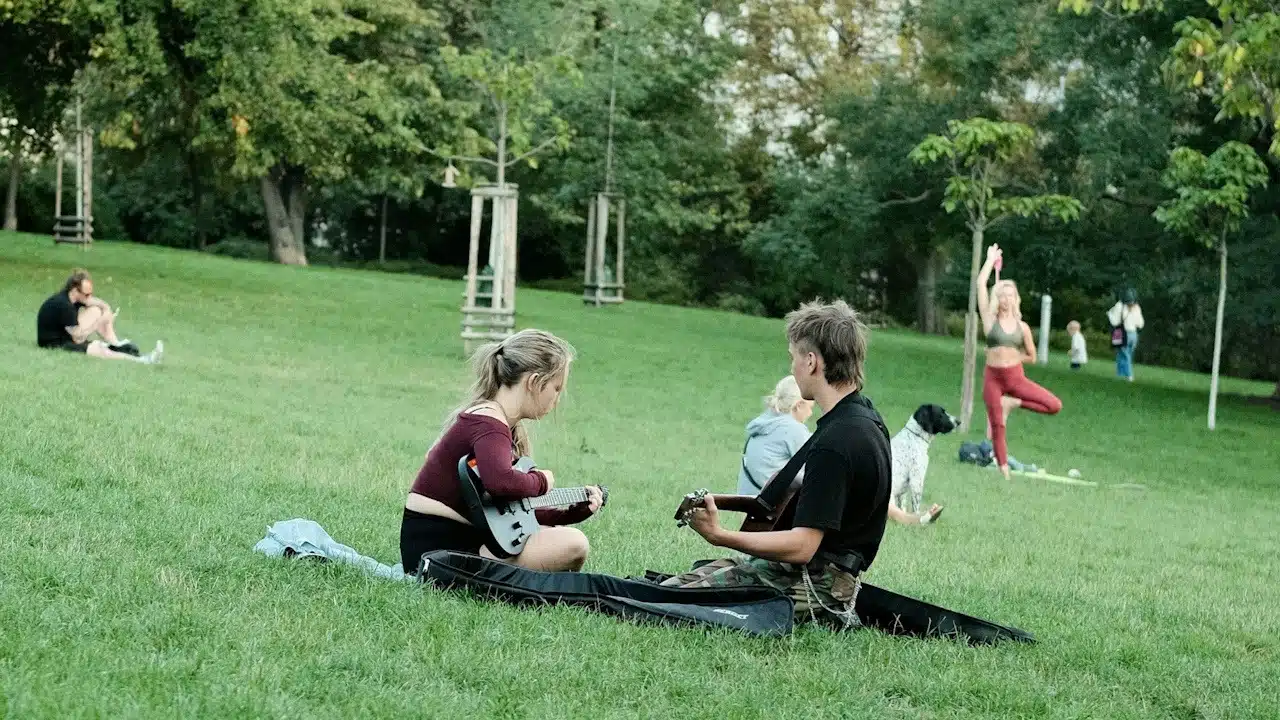 A couple playing guitar together in a park.