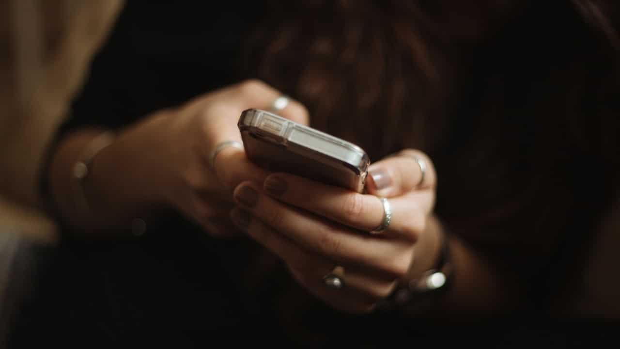A close-up shot of a person's hands, adorned with several silver rings, holding and using a smartphone.