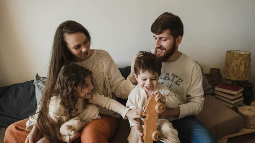A man and woman sit on a couch playing with two young children and toys.