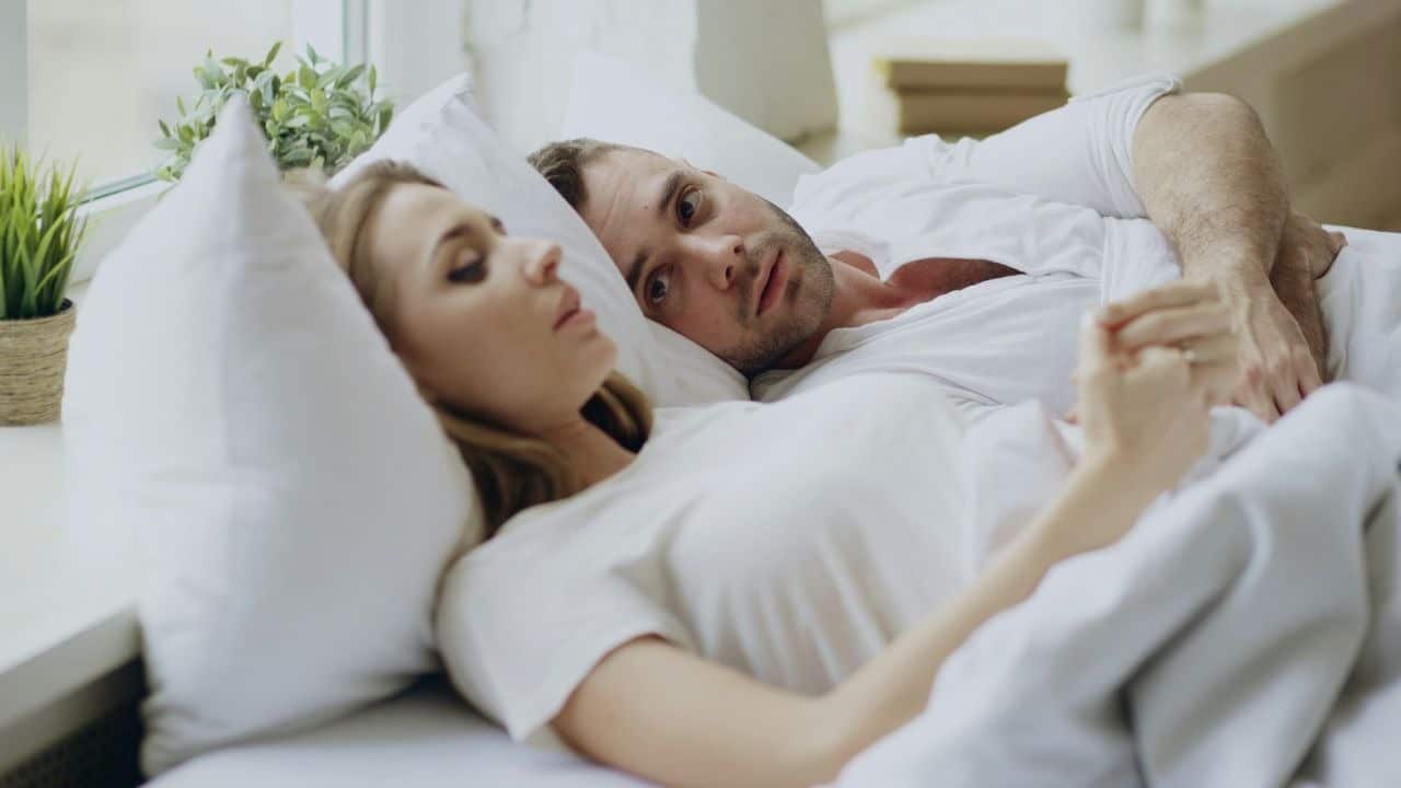 A man lies in bed looking at a woman who is looking away from him.