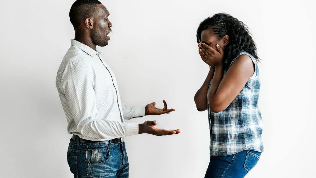 A man gestures with open palms toward a woman who is covering her face with hands.