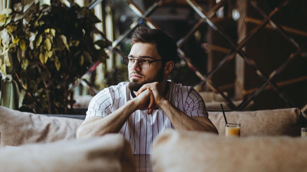 A bearded man wearing glasses and a striped shirt sits at a table in a cafe.