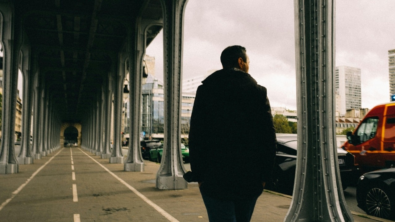 A person in a dark coat walks through a long, pillared walkway next to a street.