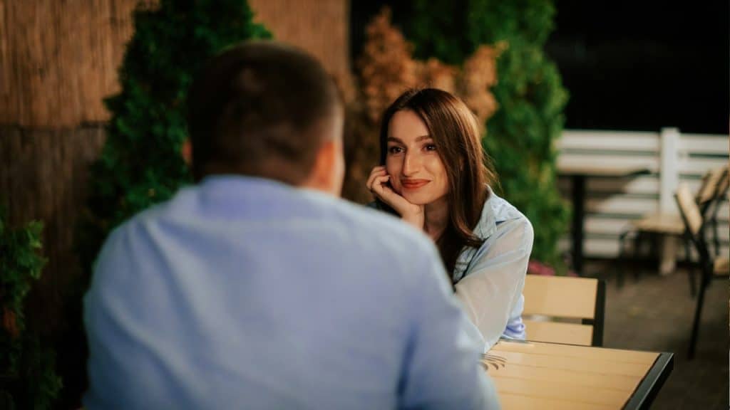 A romantic woman looking in the eys of a man sitting with her at a table in a restaurant.