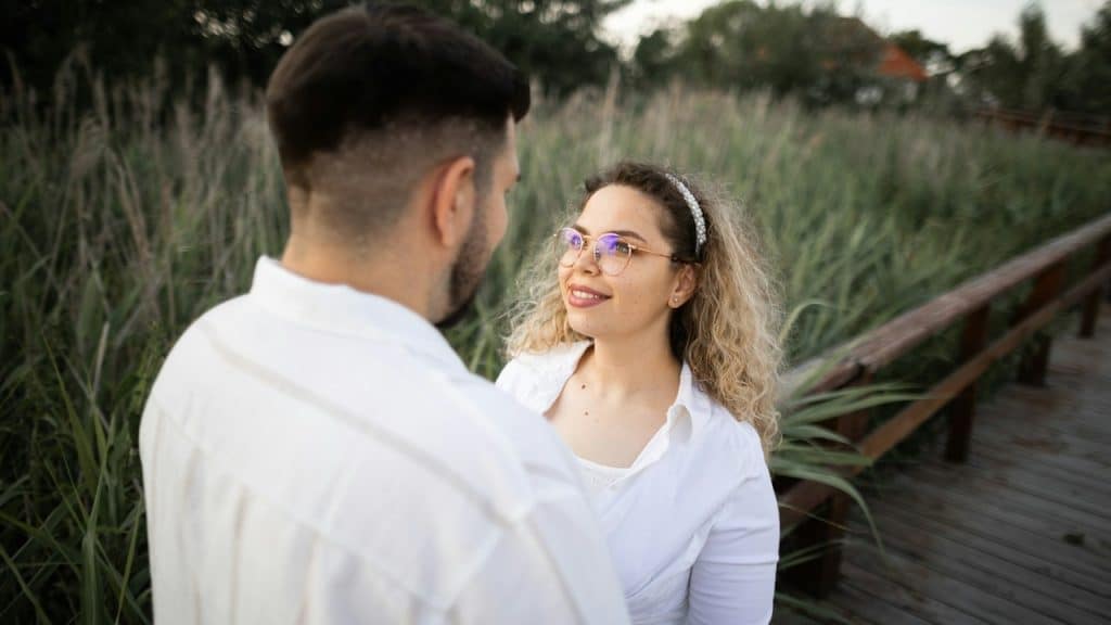 A woman with curly hair wearing glasses is looking in the eyes of a man standing next to her.