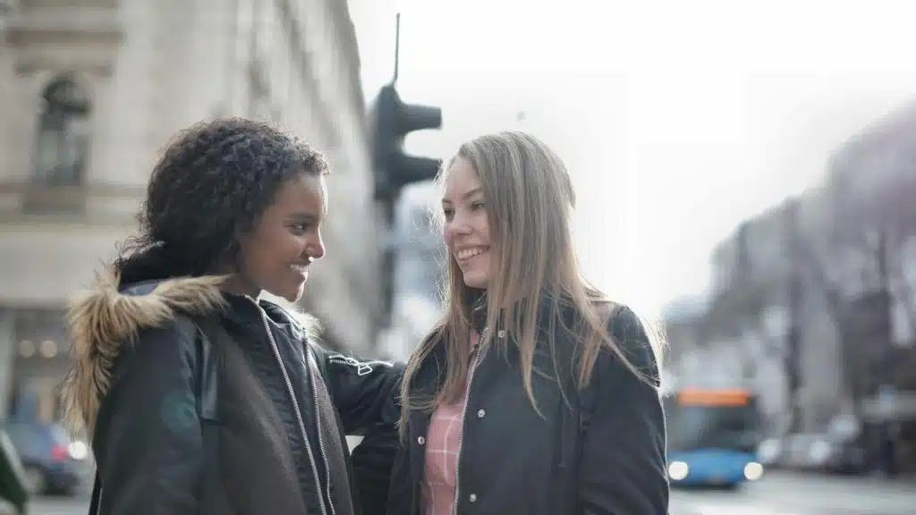 A pair of friends smiling and talking together on a city street.