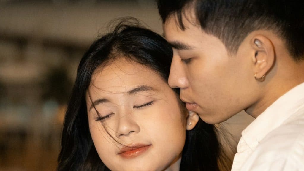 A couple in a close embrace, with one person leaning in to kiss the other’s temple.