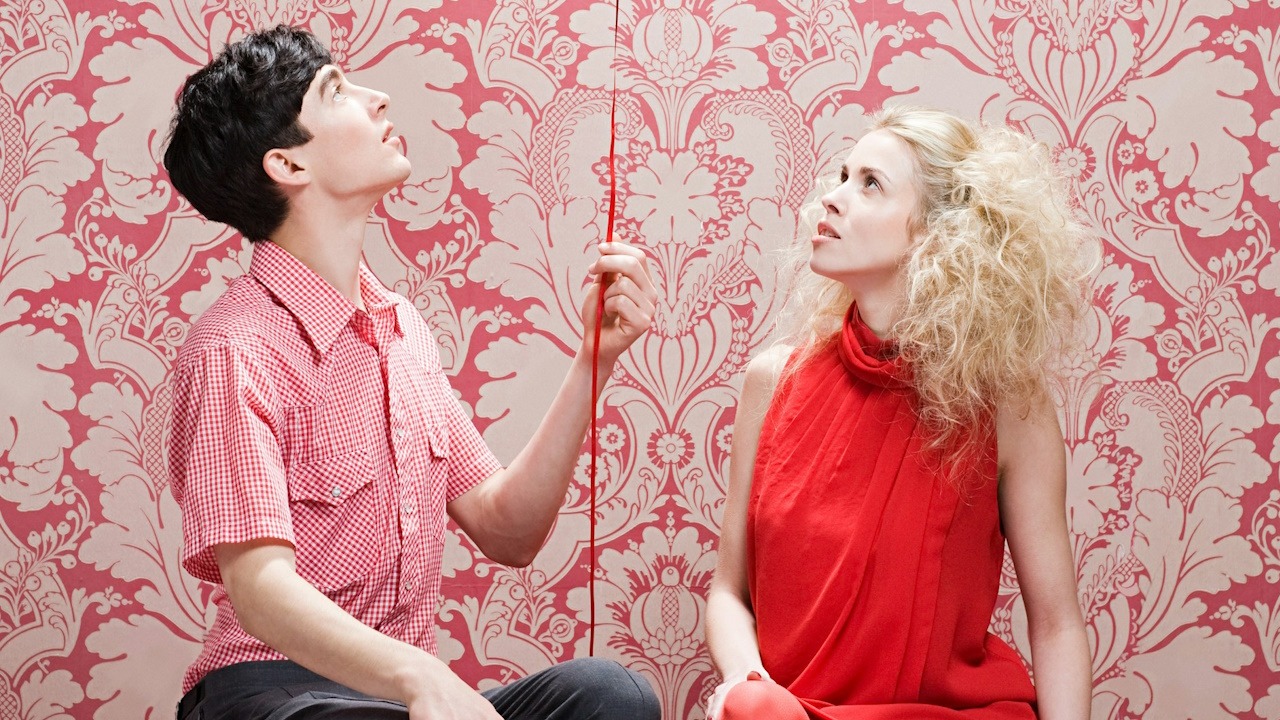 A man and a woman sitting on a bench with a balloon.