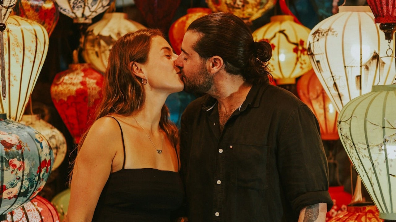 A man and a woman kissing in front of a wall of lanterns.