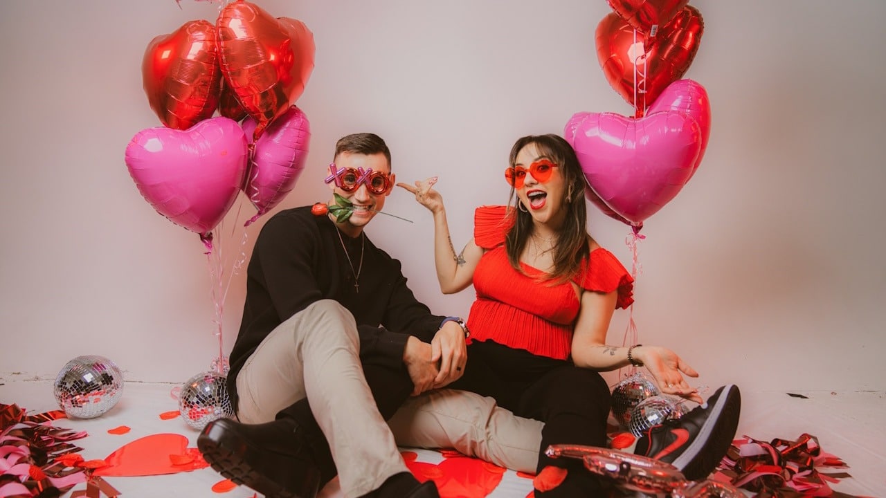 A man and a woman sitting on a floor with balloons and confetti.
