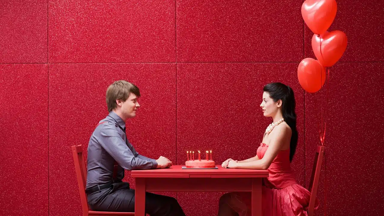 A man and woman sitting at a table with red balloons.