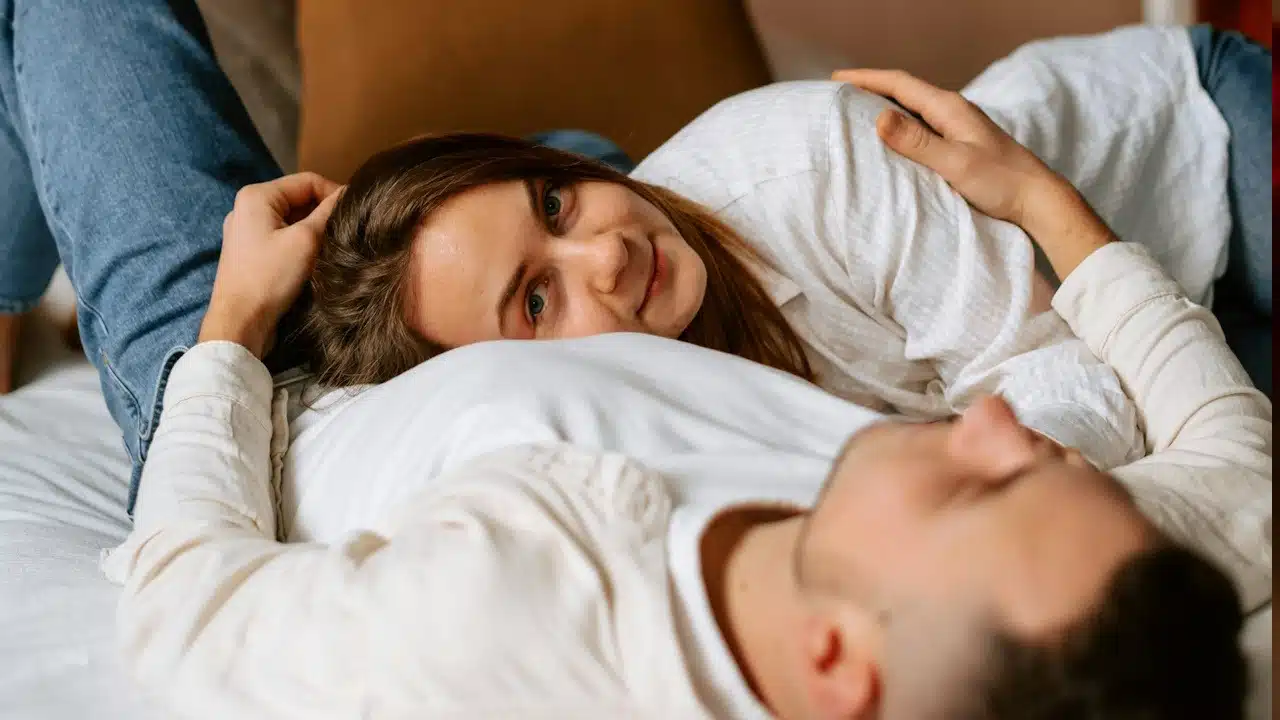 A woman lying on her husband’s lap while they are on their bed.