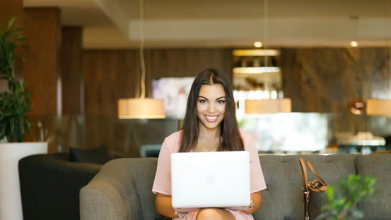 A woman smiling and using a laptop while sitting on a couch in an office.