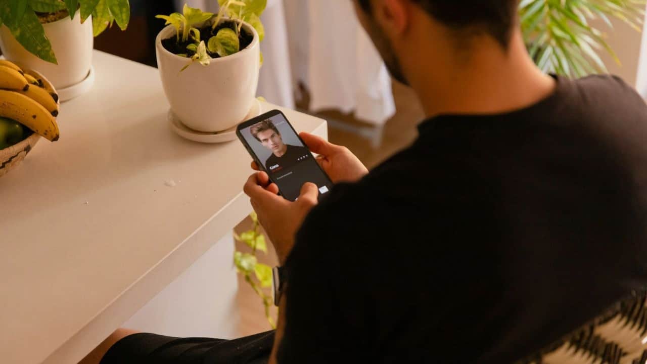 Over-the-shoulder view of a man looking at a dating profile on a smartphone at a table.