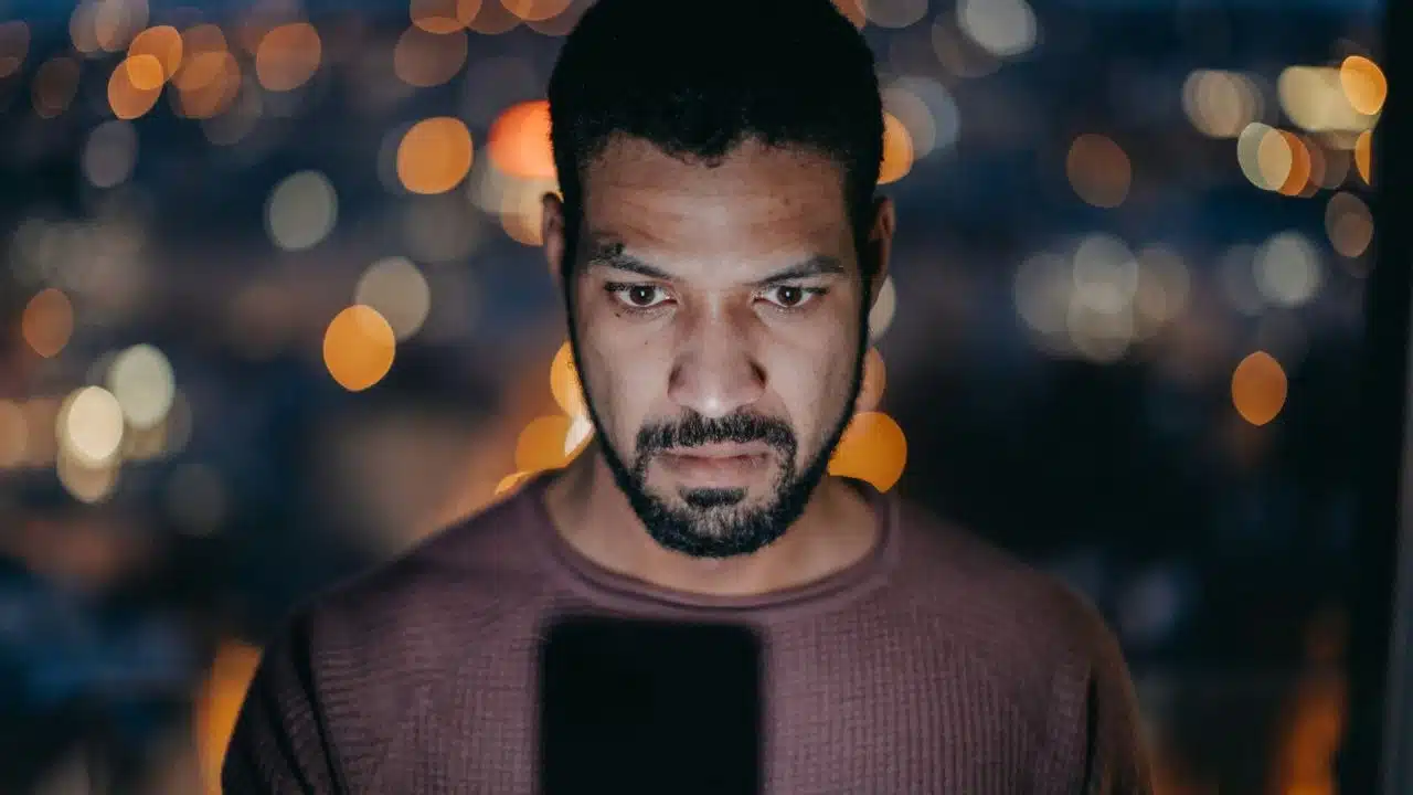 A man’s face is centered and lit from below by the glow of a smartphone screen.