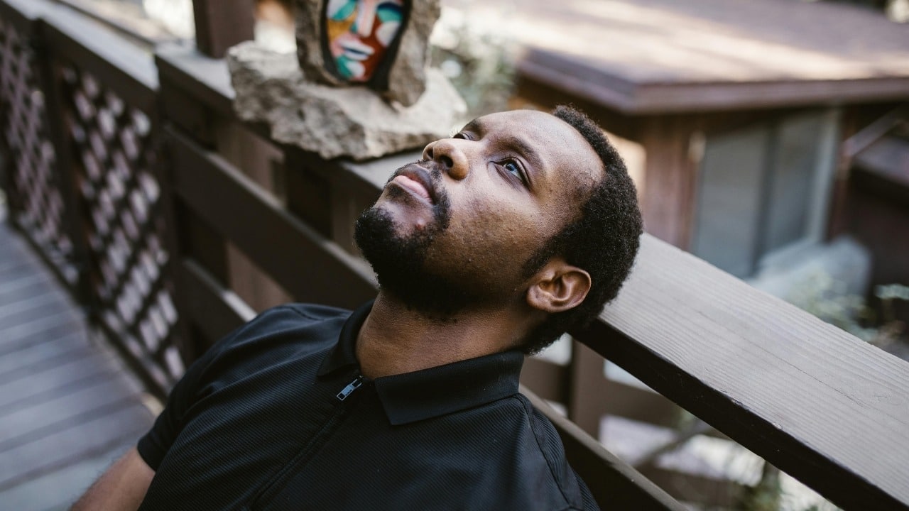 A man in a black polo shirt leans against a wooden railing and looks upward.