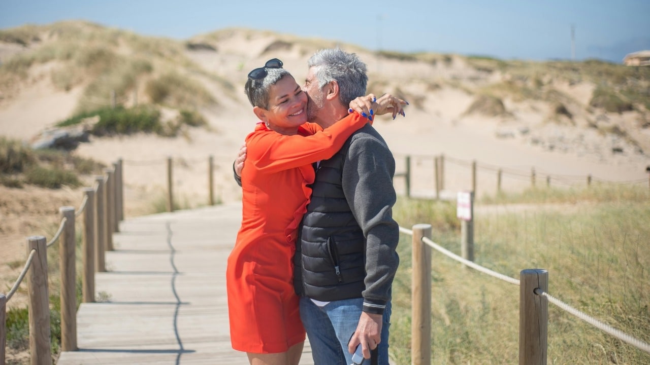 A woman in an orange dress and a man in a vest hugging outdoors.