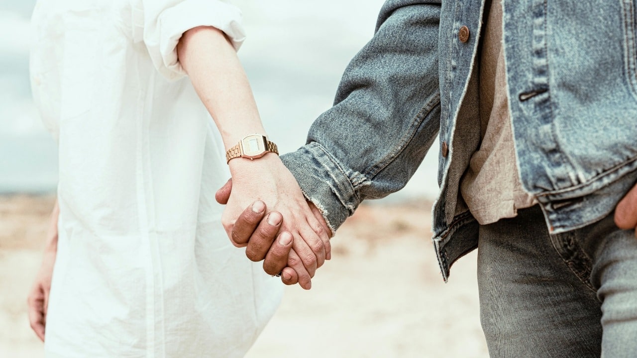 Close up view of two people holding hands while walking outside in a natural setting.