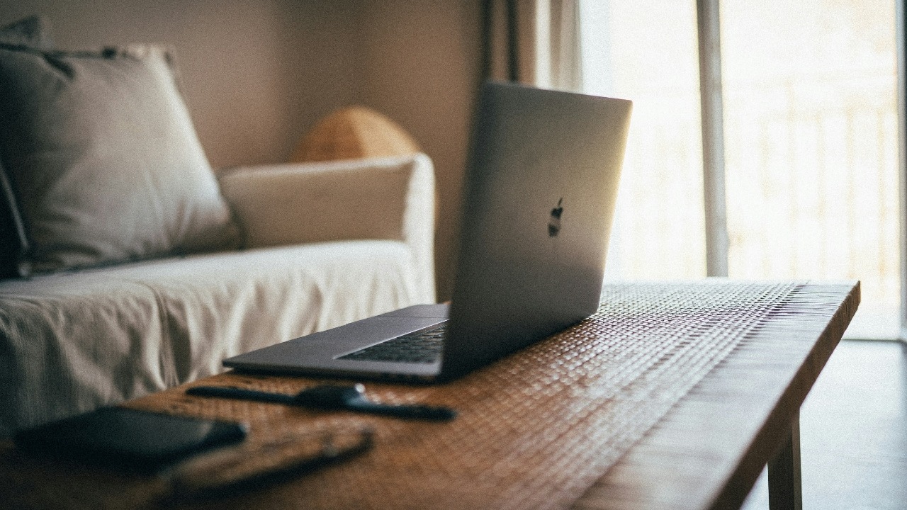A laptop sits open on a wooden table in a dimly lit living room setting.