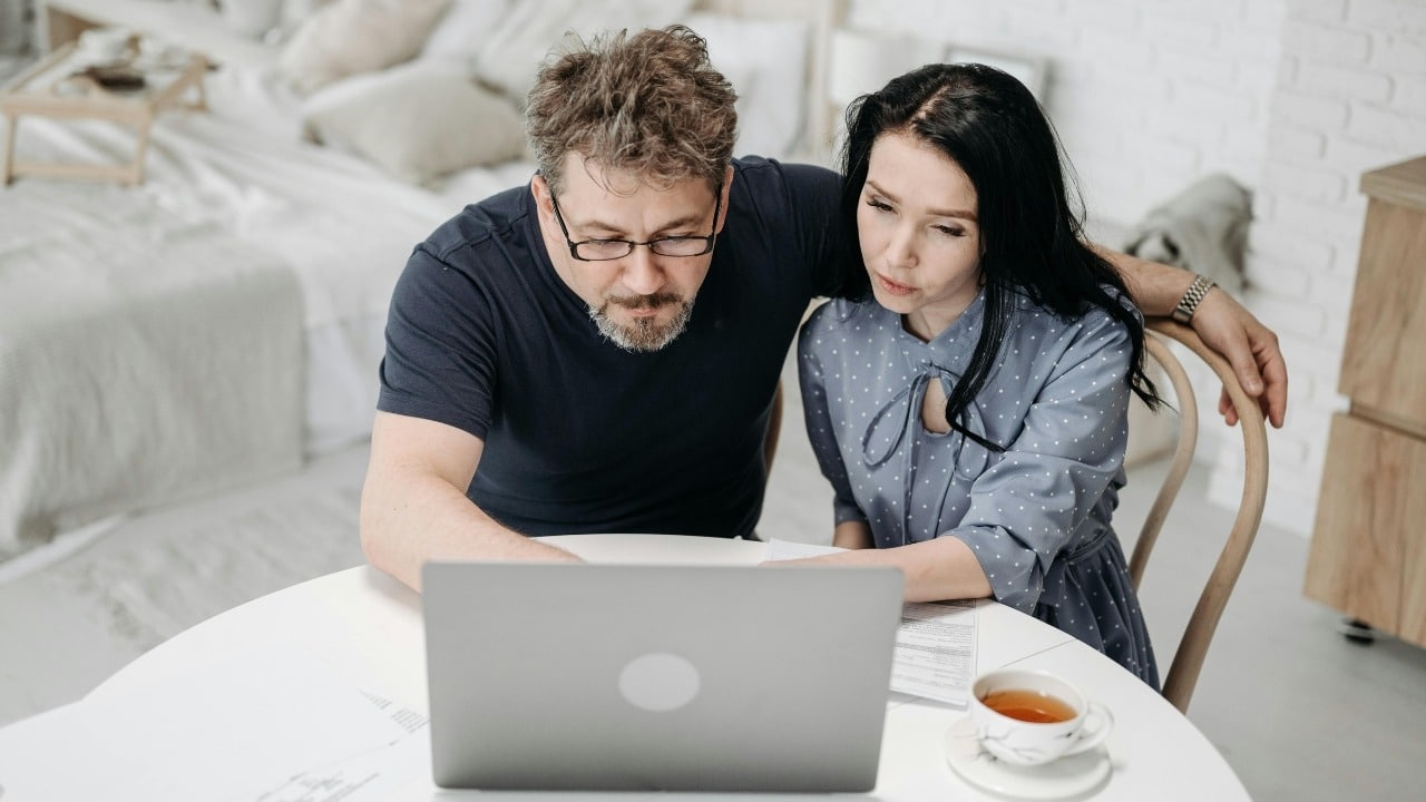 A man and woman looking closely at a laptop screen together while sitting at a table.