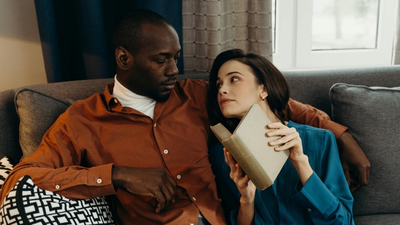 A man and woman sitting on a sofa looking at each other, woman holding a book.