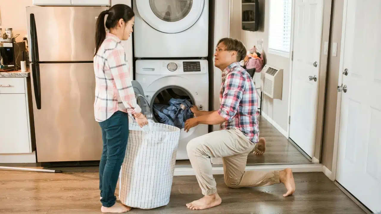 A man and woman doing laundry together in a kitchen with a stacked washer-dryer.
