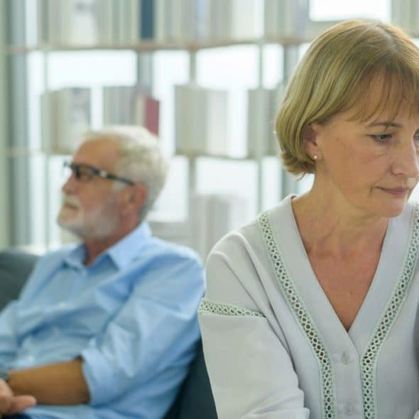 A senior man and woman sitting on a sofa looking in different directions indoors.