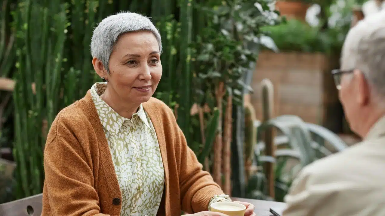 A senior woman with short gray hair smiling while talking to someone at a table.