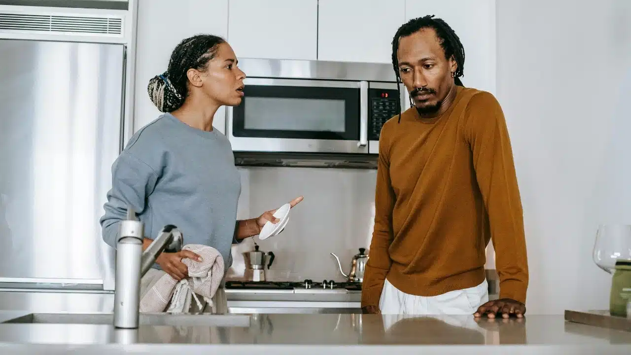 A woman talking to a man in a kitchen while holding a white saucer plate.