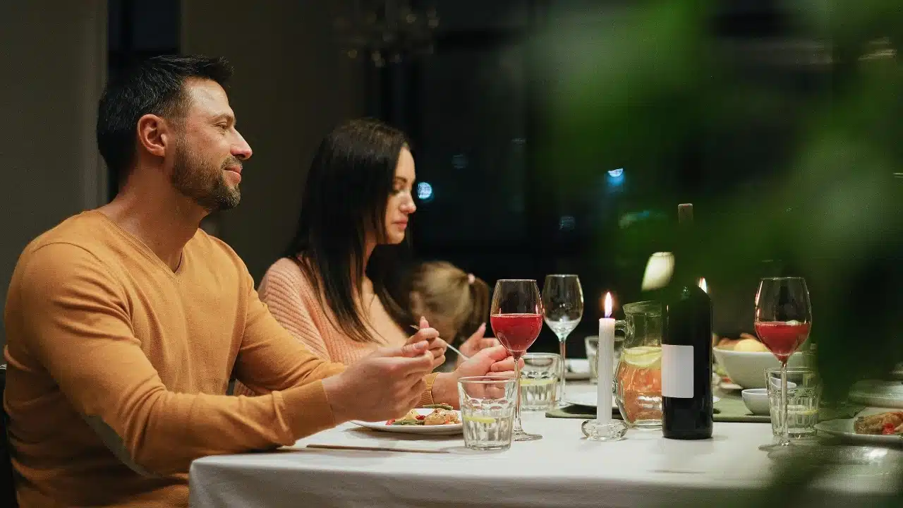 A man and woman sitting at a dinner table with wine glasses and a candle.
