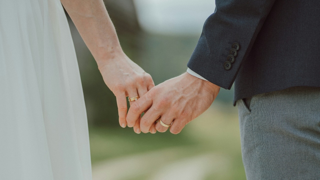 Close up of a man and woman holding hands while wearing gold colored wedding bands.