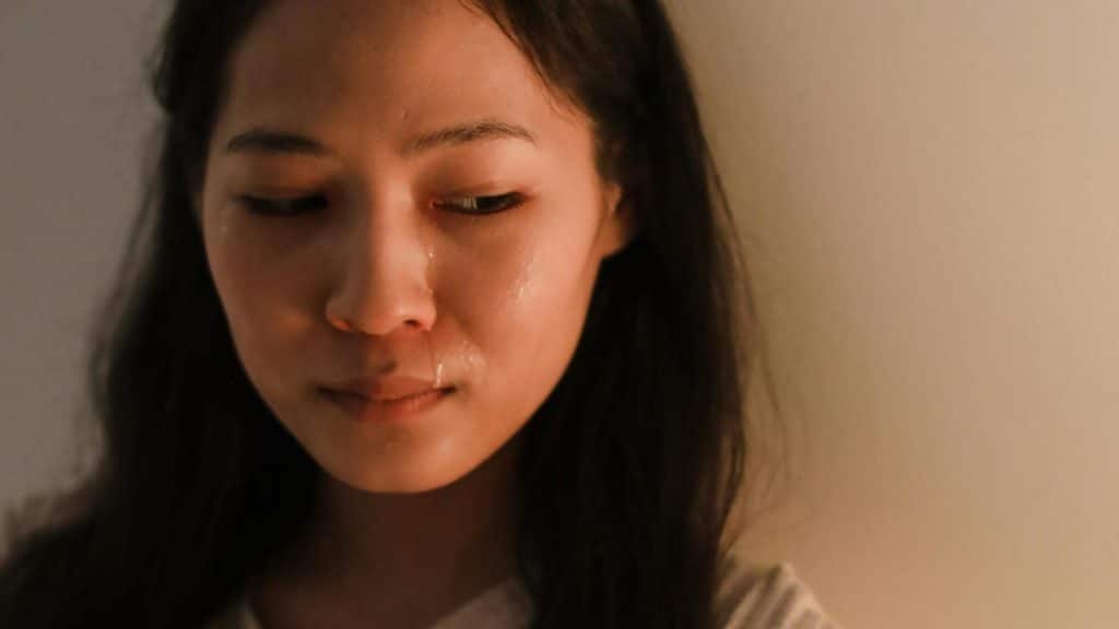 A woman looks down with tears on her face in soft light.
