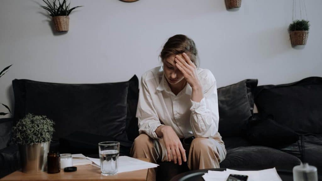 A stressed person sits on a couch with papers scattered on a table.