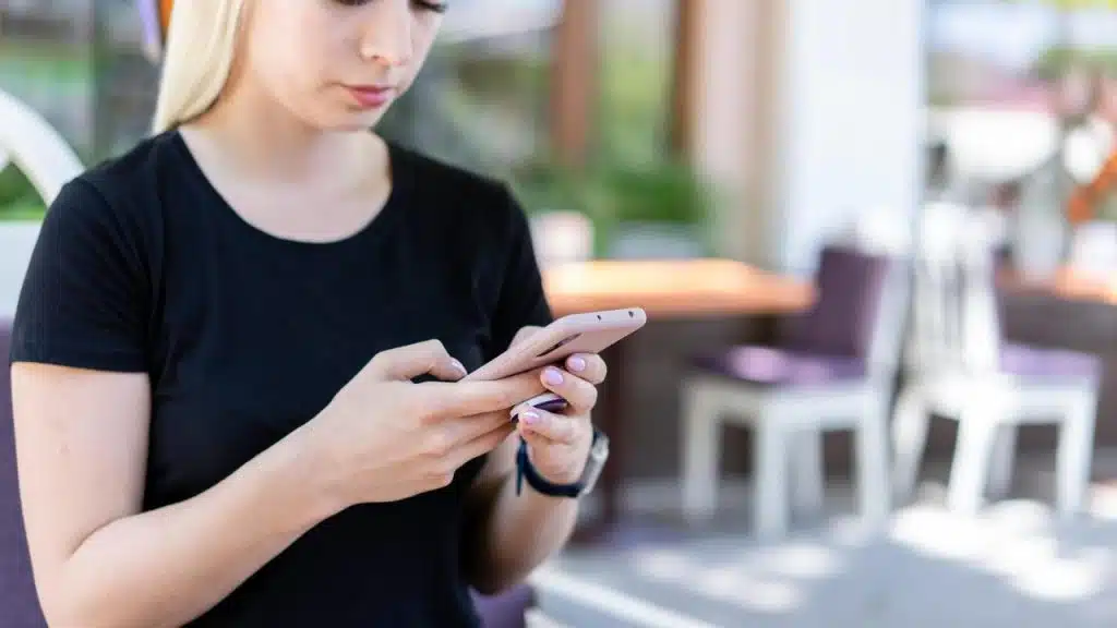 A woman standing outdoors and using a smartphone.