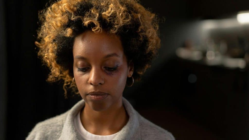 A woman with curly hair looking down with a sad expression.