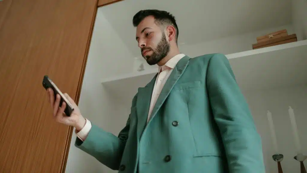 A man in a teal suit looks at his phone indoors.